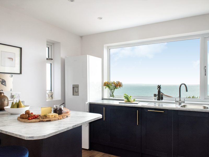 Close up view of the kitchen window over looking the sea, with the fridge on the left